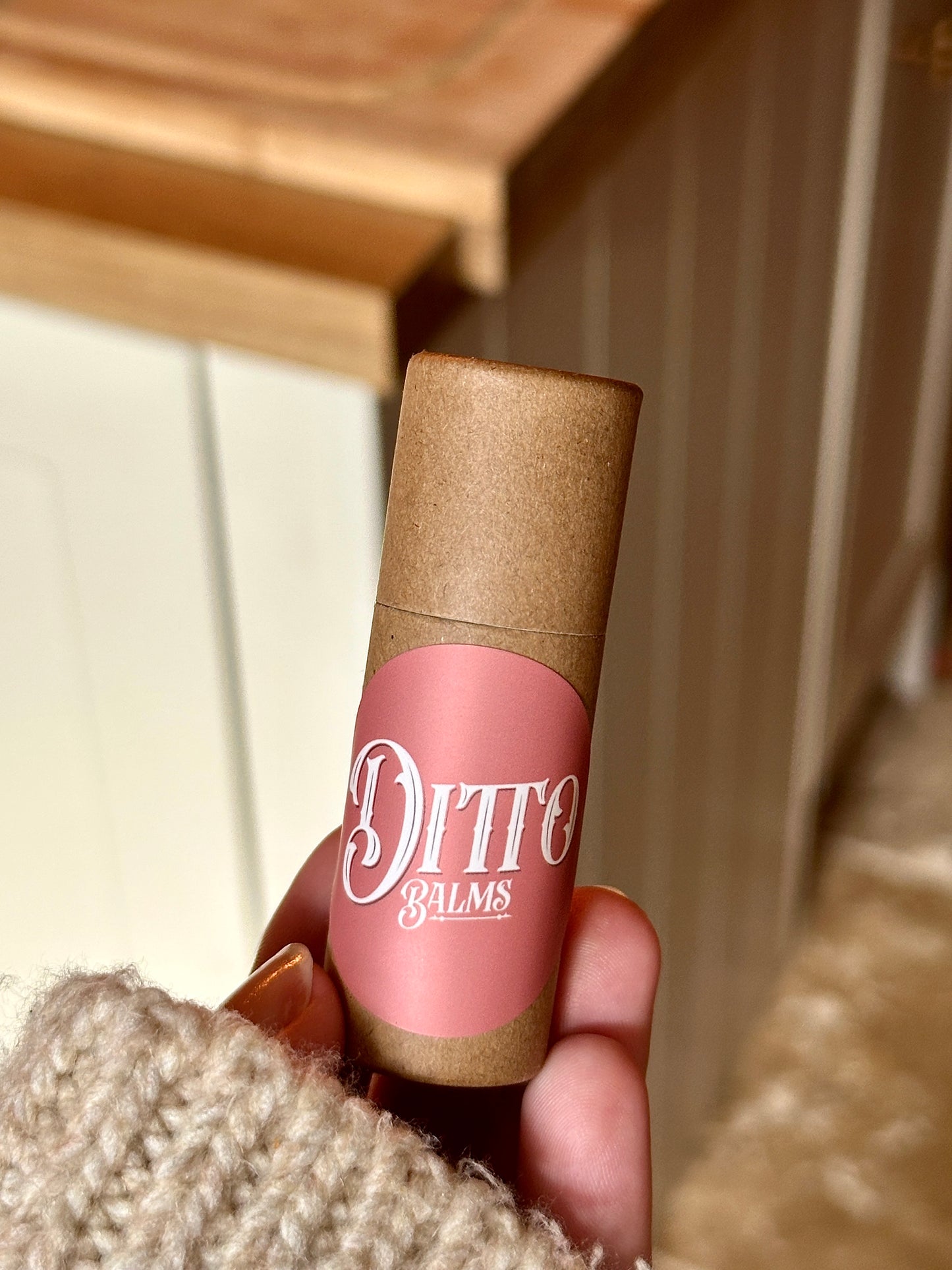 Hand holding a Ditto Balms solid perfume with a wooden surface in the background
