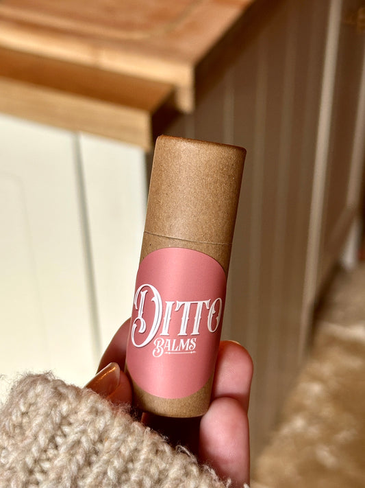 Hand holding a Ditto Balms solid perfume with a wooden surface in the background